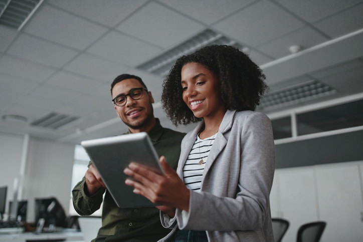 Portrait of smiling professional young African American businesswoman showing data on digital tablet to male colleague in office