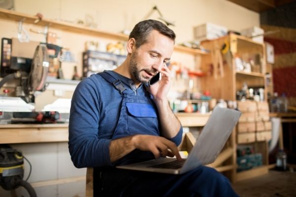 Working man sitting at table with Notebook Computer while on a cell phone call.