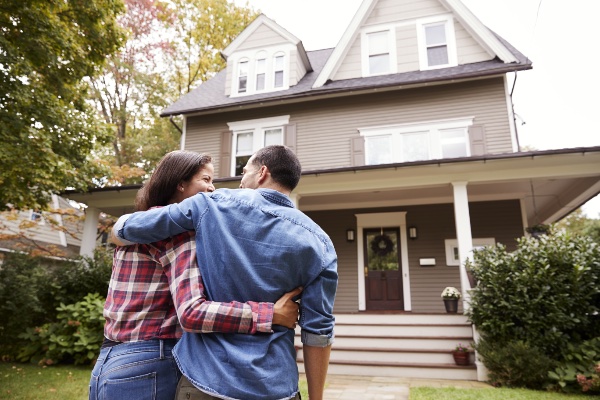 Wife and Husband arms hold each other while standing in front of their new house