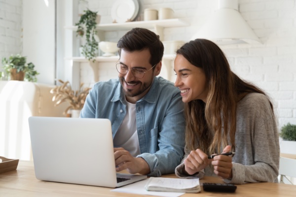 Smiling Man on Notebook computer while daughter smiles looking to the left of at Notebook Computer screen while holding a pen.